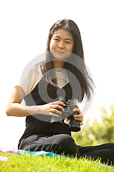 Asian young woman sit on mound seeking binoculars .